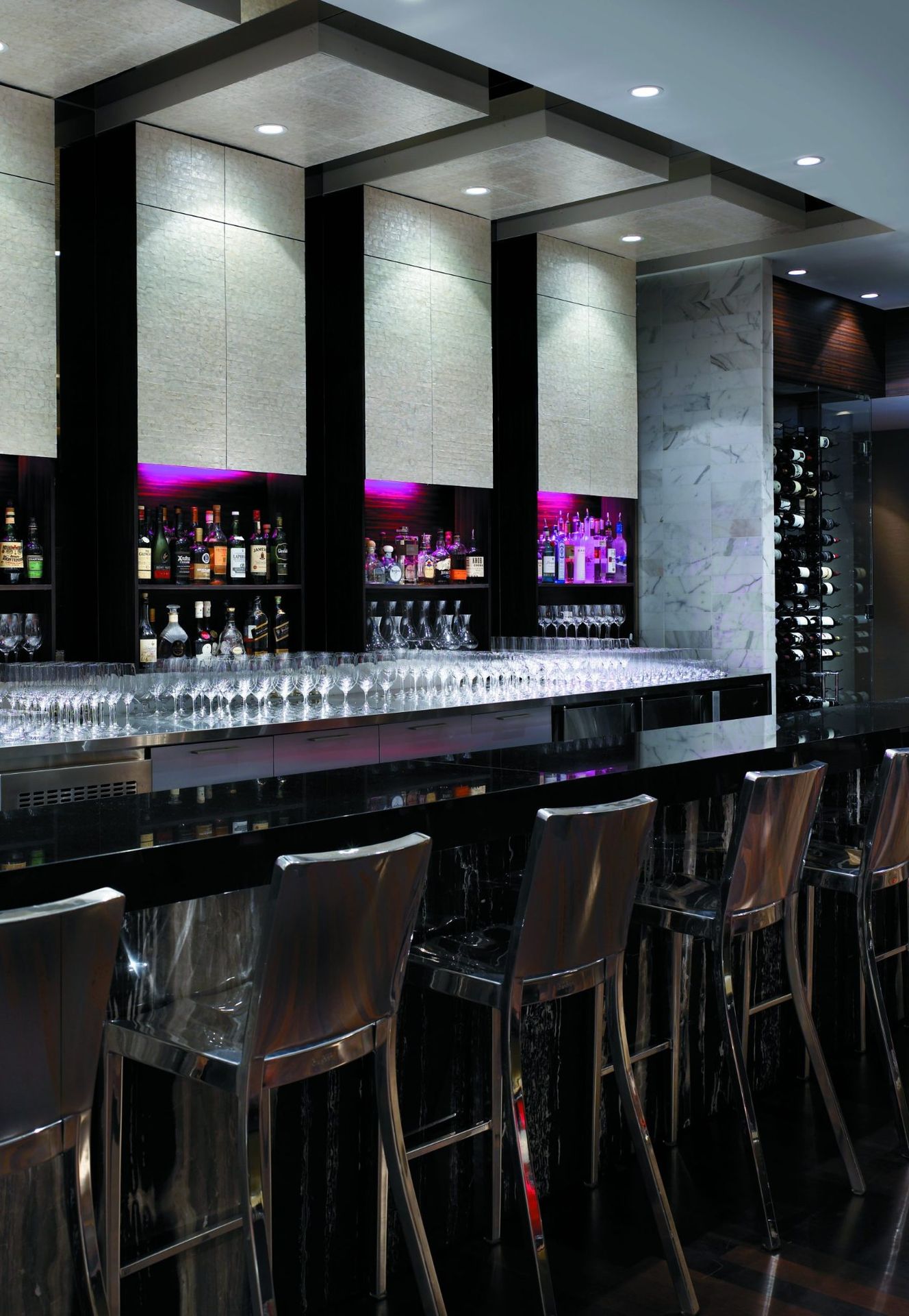 Recessed downlights washing textured stone panels above a hotel bar