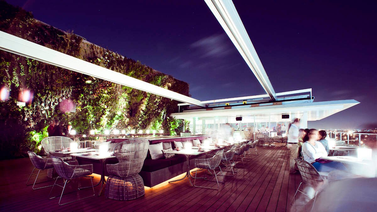 Juvia rooftop terrace in Miami at night, with a living green wall grazed from below and warm low-level light at the tables