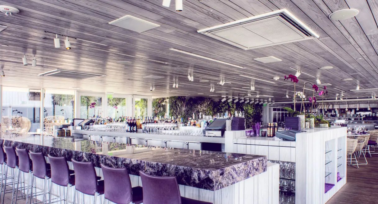 The bar at Juvia, with white track heads on a whitewashed timber ceiling above a marble bar