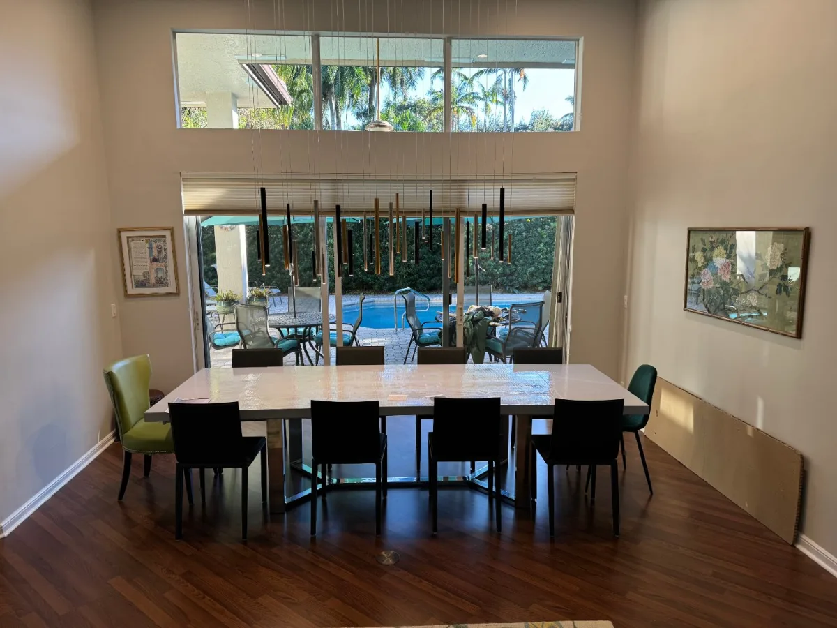 Dining room in a Miami residence with a cluster of slim black and brass cylinder pendants at staggered heights